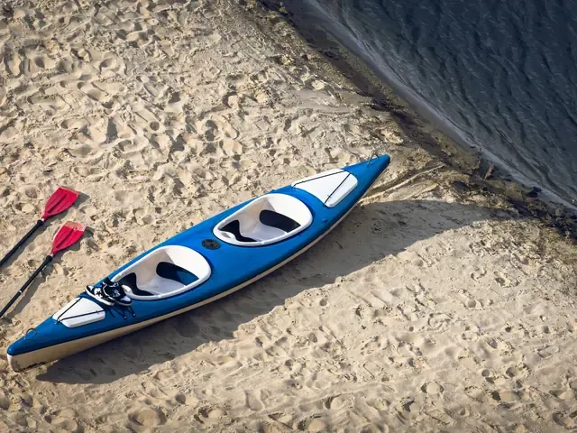 Un kayak et deux pagaies posés sur le sable, vus du dessus